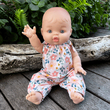 Baby doll in spring floral romper sitting in a garden waving