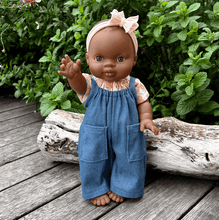 Doll wearing a blue denim overalls with a peach headband in a natural setting