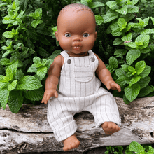Baby doll in overalls sitting on a log with green foliage in the background