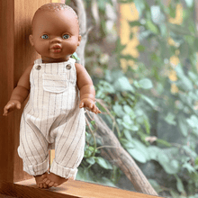 Baby Doll wearing white pinstripe overalls standing on a wooden surface with a blurred natural background