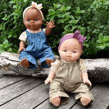 Two dolls sitting on a wooden log with a green leafy background