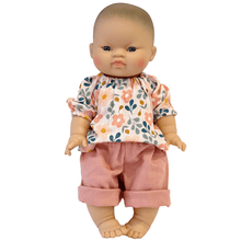 Baby doll wearing a floral top and pink pants on a white background