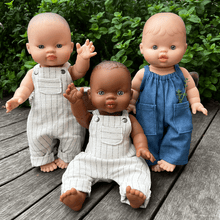 Three dolls in overalls on a wooden surface with a green leafy background