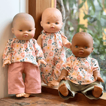 Three dolls with different skin tones wearing floral outfits on a wooden surface.